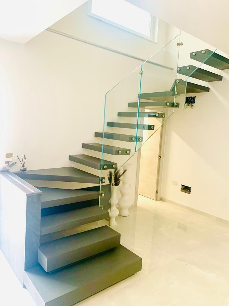 Scala moderna con ringhiera in vetro e gradini grigi in una stanza bianca.