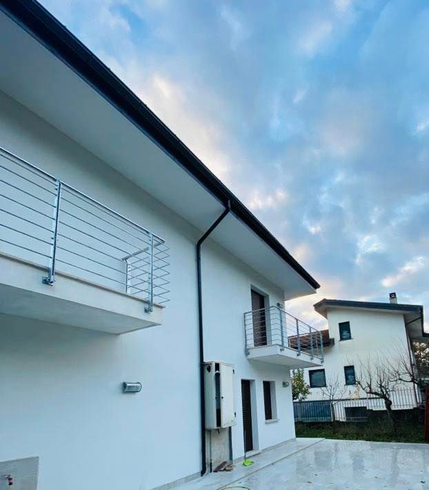 Casa bianca moderna con balconi, ringhiere metalliche, grondaie nere e cielo coperto.