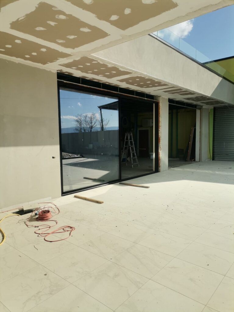 Cantiere con grande porta a vetri con cornice nera, vista interna. Pareti, soffitto e pavimento non finiti.