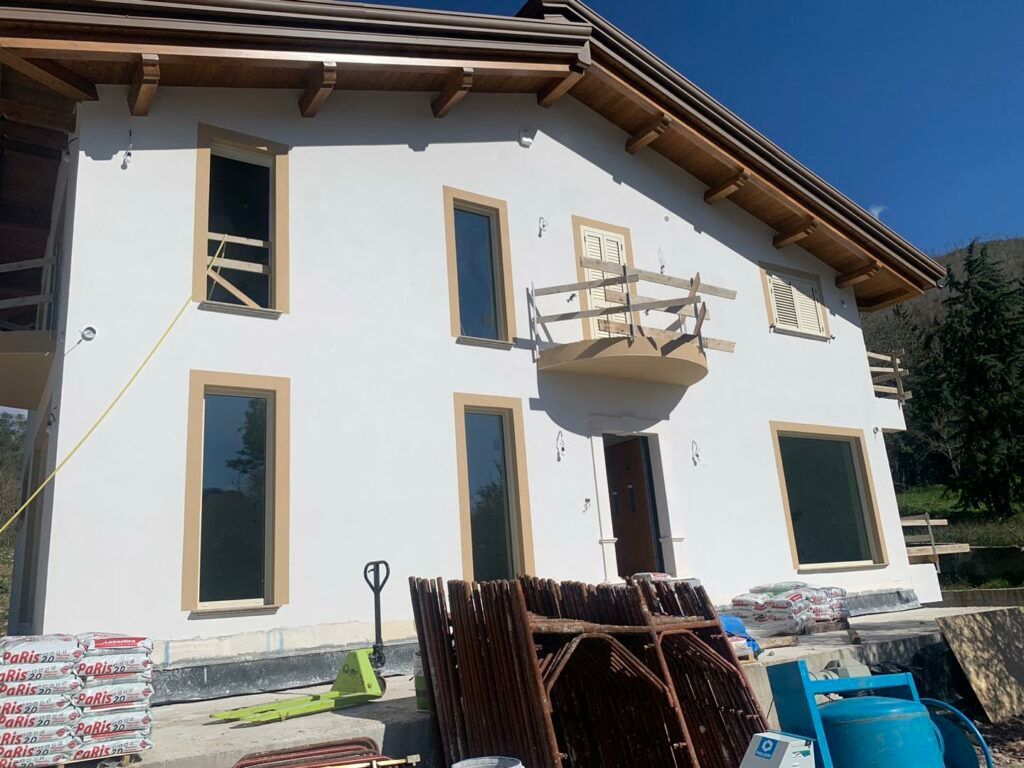 Casa a due piani con pareti in stucco bianco e finiture marroni attorno alle finestre. Materiali da costruzione sulla facciata.