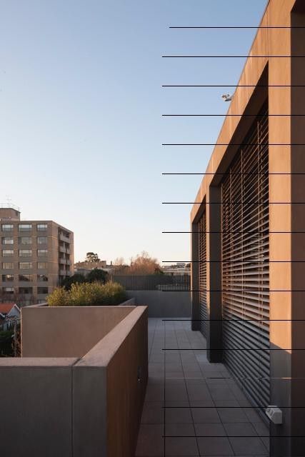 Terrazza panoramica con pareti in cemento, linee metalliche e finestre ombreggiate sotto un cielo limpido; contesto urbano.