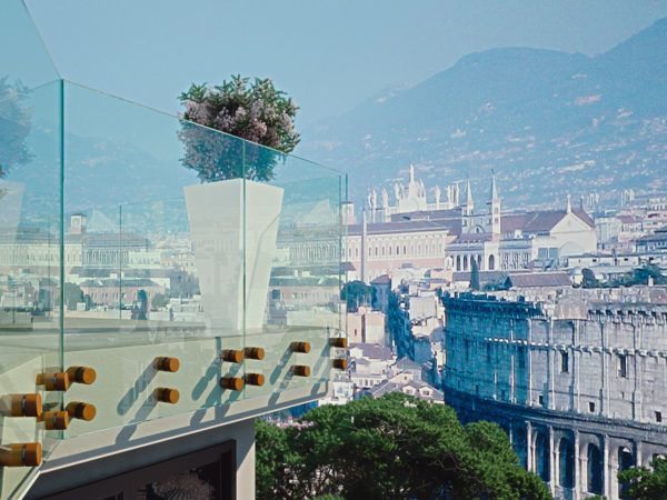 Balcone in vetro con una fioriera bianca piena di fiori, con vista sulla città e sulle montagne.