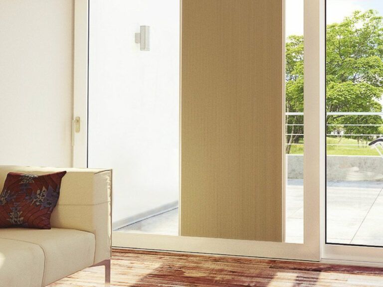 Tende a pannello beige che coprono una porta scorrevole in vetro, con un divano bianco e vista esterna sugli alberi.