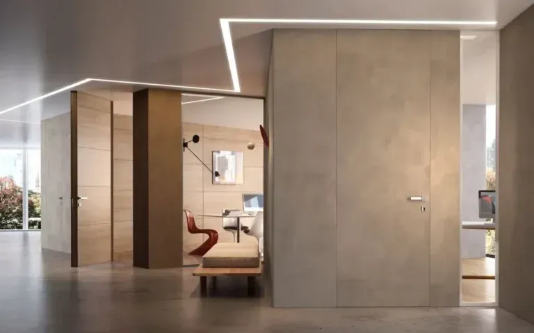 Interni moderni con pareti e porte dai colori chiari. Spazio ufficio con sedia e scrivania rosse visibili attraverso un'apertura.