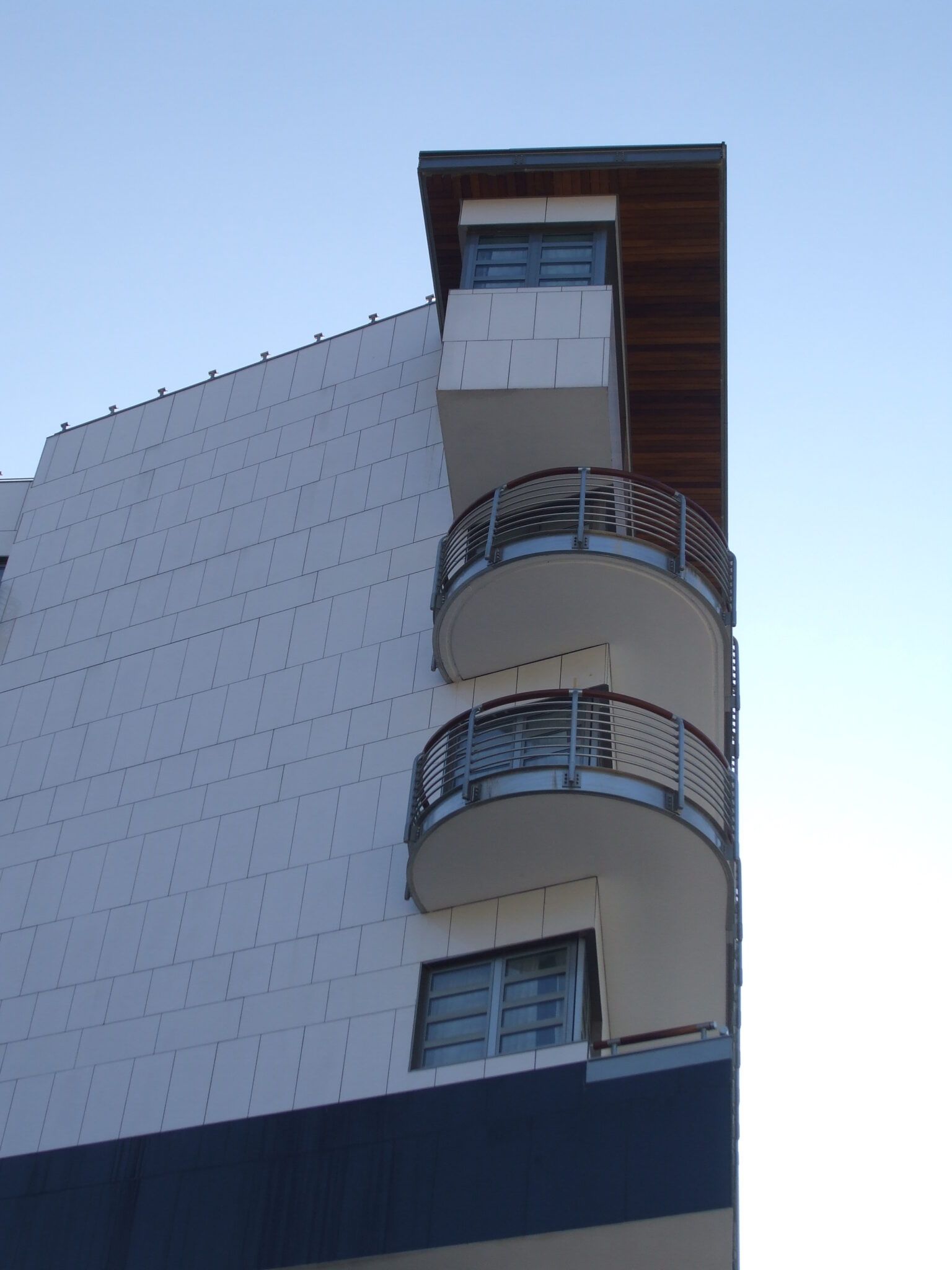 Edificio bianco con balconi curvi, cielo azzurro sullo sfondo.