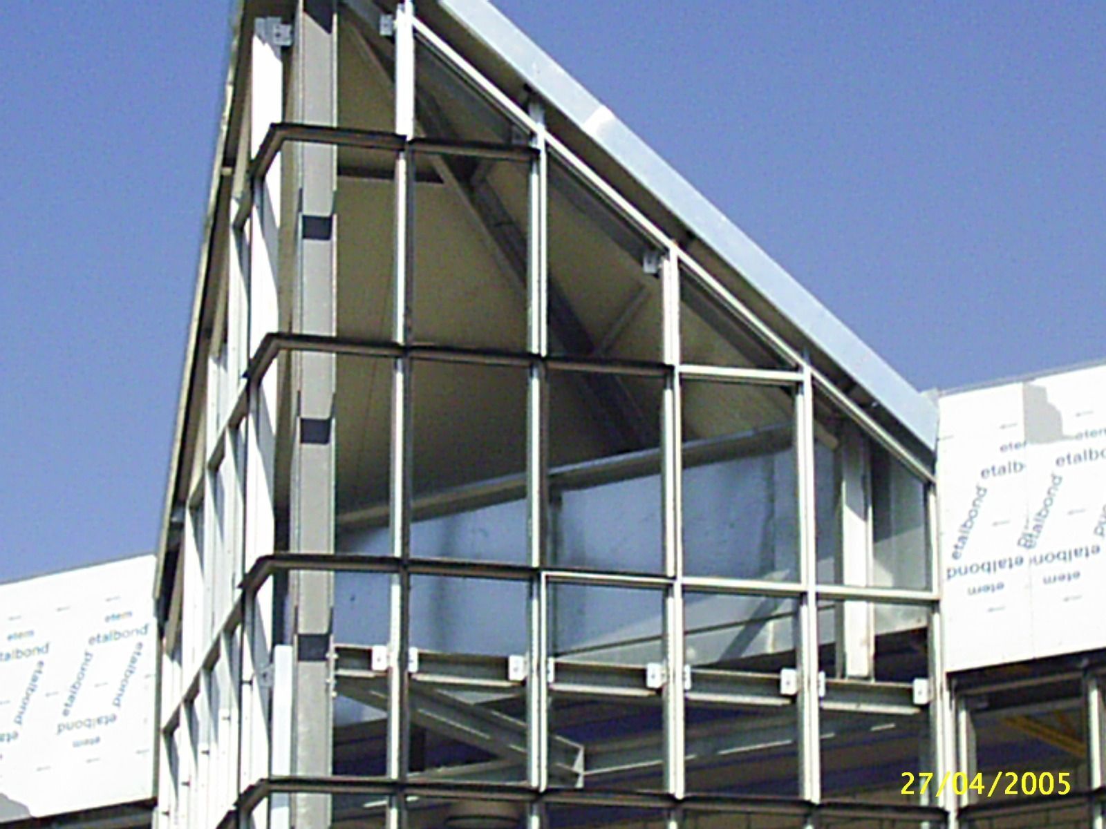 Esterno di un edificio moderno con tetto triangolare e grandi finestre in vetro; struttura in metallo.