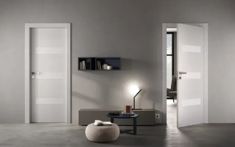 Camera moderna con due porte bianche a pannelli, una delle quali aperta, una mensola sospesa e arredi neutri.