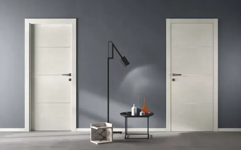 Due porte bianche con pannelli su una parete grigia con una lampada e un tavolo neri.