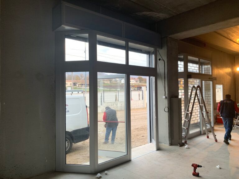 Operai che installano grandi porte in vetro in un cantiere edile. Vista interna, una porta aperta, furgone bianco all'esterno.