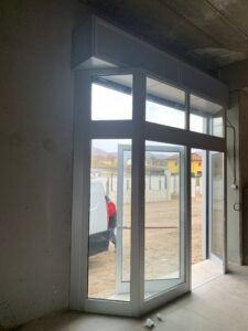 Porte in vetro in un edificio con telai bianchi e copertura superiore; all'esterno un furgone parzialmente visibile.