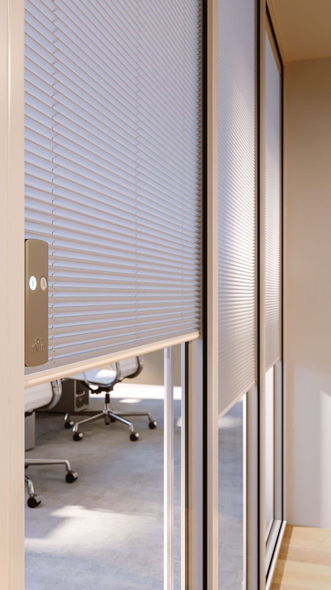 Interno dell'ufficio con tende plissettate chiare chiuse che coprono le grandi finestre, vista sull'ufficio.