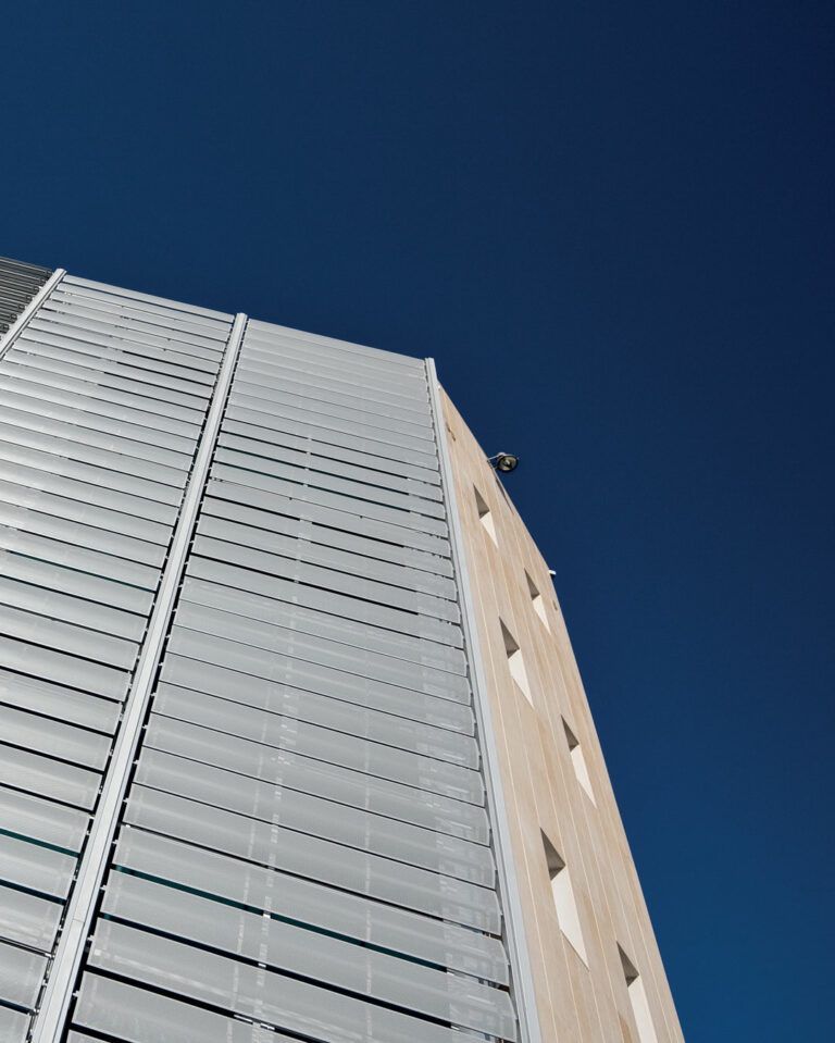 Alto edificio con pannelli metallici e di colore chiaro, contro un cielo blu intenso.