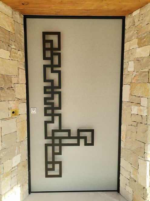 Porta d'ingresso moderna con motivo geometrico in metallo nero su vetro satinato, incorniciata da pareti in pietra.