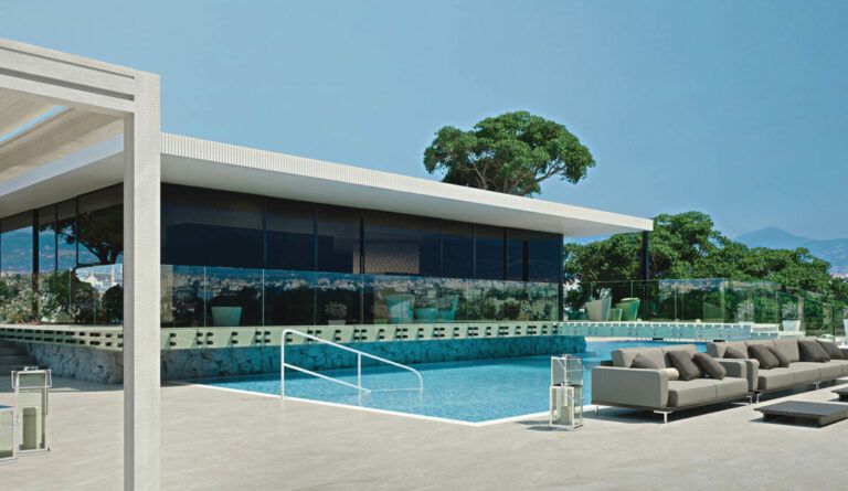 Area lounge a bordo piscina con edificio, piscina e posti a sedere. Giornata di sole.