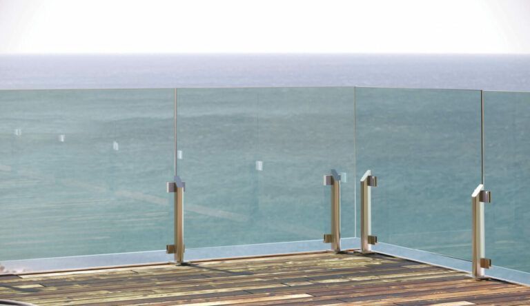 Ringhiera in vetro con vista sull'oceano, fissata a una terrazza in legno.