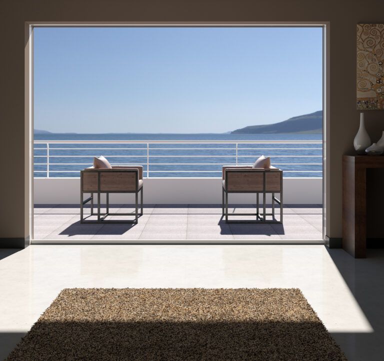 Portafinestra aperta con vista sull'oceano, due sedie e un tappeto all'interno di una stanza.