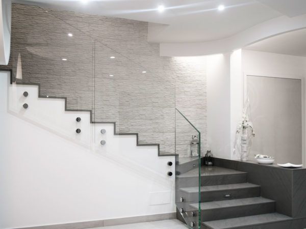 Scala moderna con ringhiera in vetro e parete grigia testurizzata.