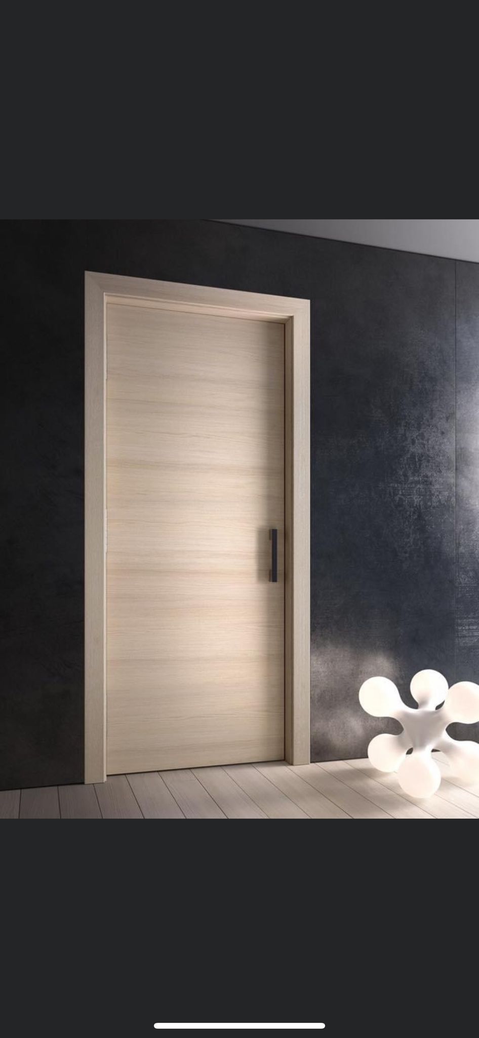 Una porta di legno chiaro con una maniglia scura, appoggiata su una parete dalla texture scura.