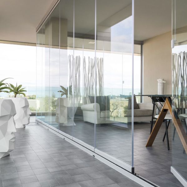 Balcone con pareti in vetro e vista sull'oceano, arredato con mobili moderni e pavimento in piastrelle grigie.