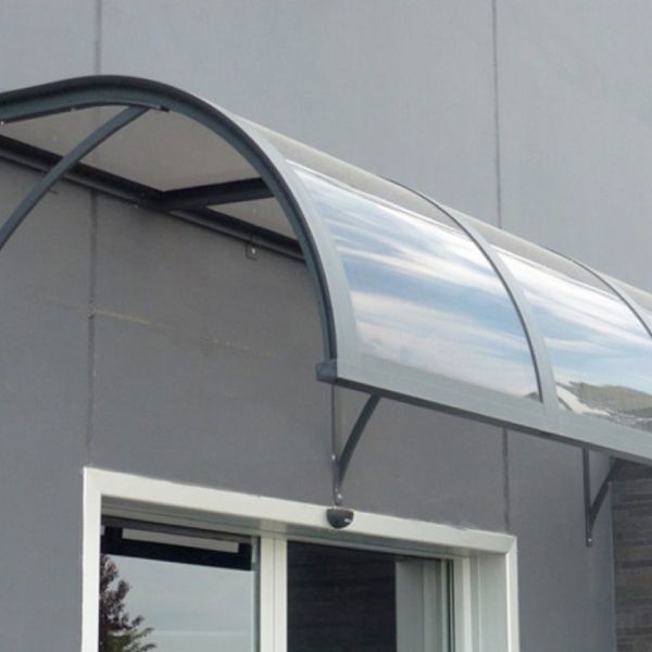 Tenda curva e trasparente sopra una finestra e una porta di un edificio grigio.