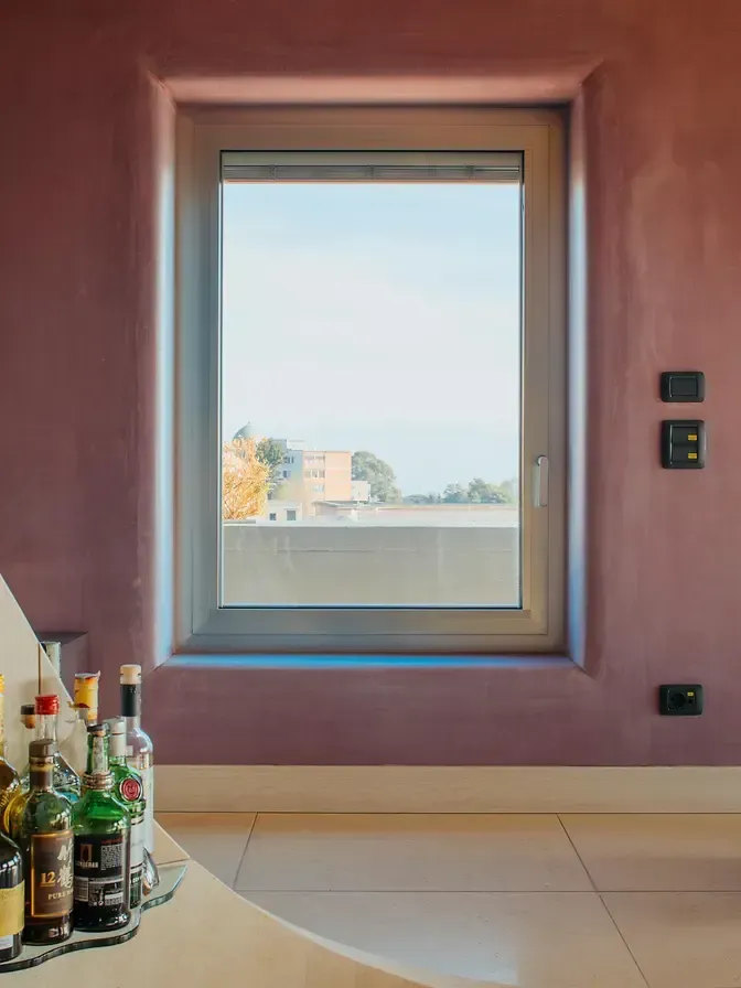 Vista dalla finestra sul paesaggio urbano e sull'oceano. La finestra ha una cornice chiara ed è incastonata in una parete viola.
