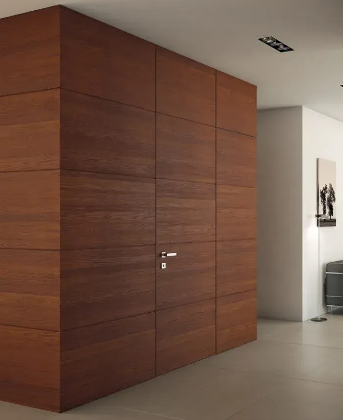 Porta con pannelli in legno in un ambiente moderno; maniglia della porta visibile, pareti bianche e pavimento chiaro.