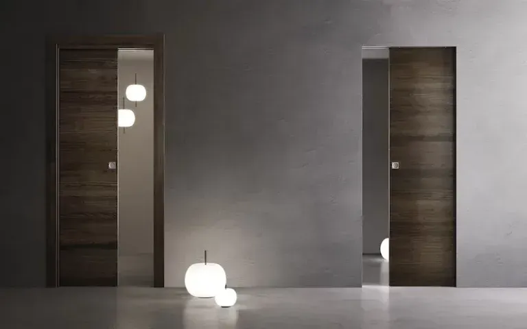Due porte scorrevoli in legno incastonate in una parete grigia, illuminate da lampade da terra rotonde e luminose.