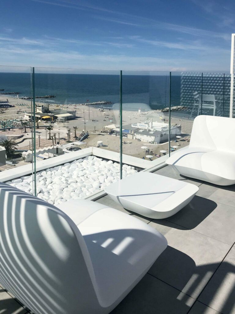 Patio sul tetto con mobili bianchi, dettagli in pietra bianca e vista sulla spiaggia e sull'oceano.