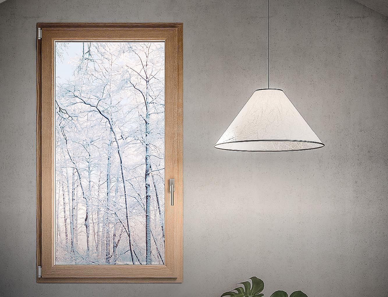 Finestra con alberi innevati, cornice in legno e lampada sospesa su una parete grigia.