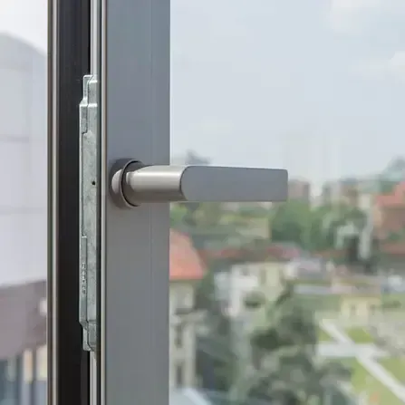 Maniglia argentata su telaio grigio, parzialmente aperta su una vista sfocata della città.