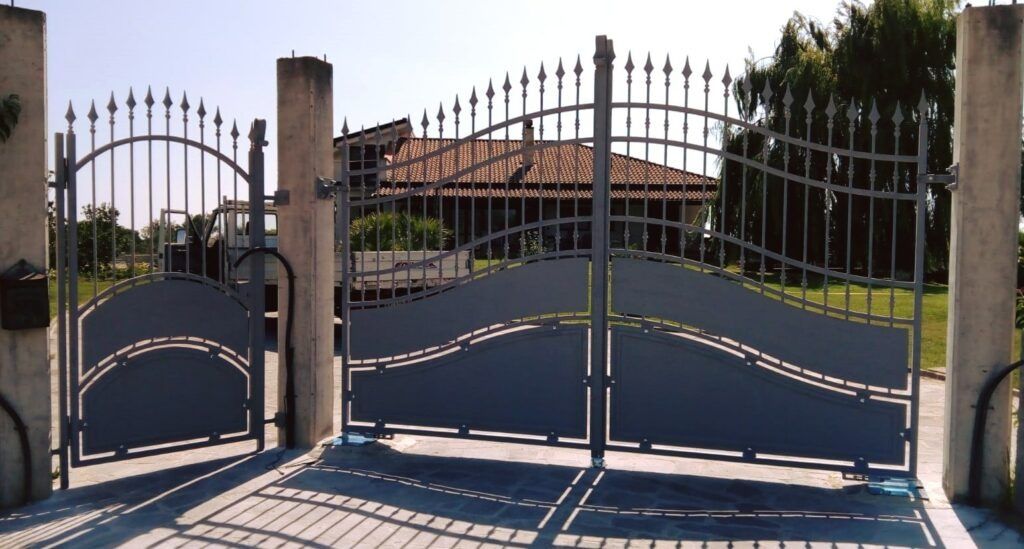 Cancello d'accesso in metallo grigio con archi decorativi, di fronte a una casa.