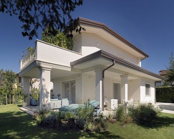 Casa bianca a due piani con colonne, veranda, balcone e prato verde in una giornata di sole.