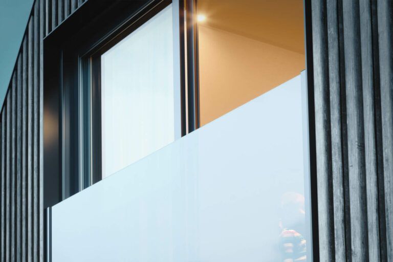 Vista esterna dell'edificio con rivestimento in legno scuro, finestra con luce interna intensa.