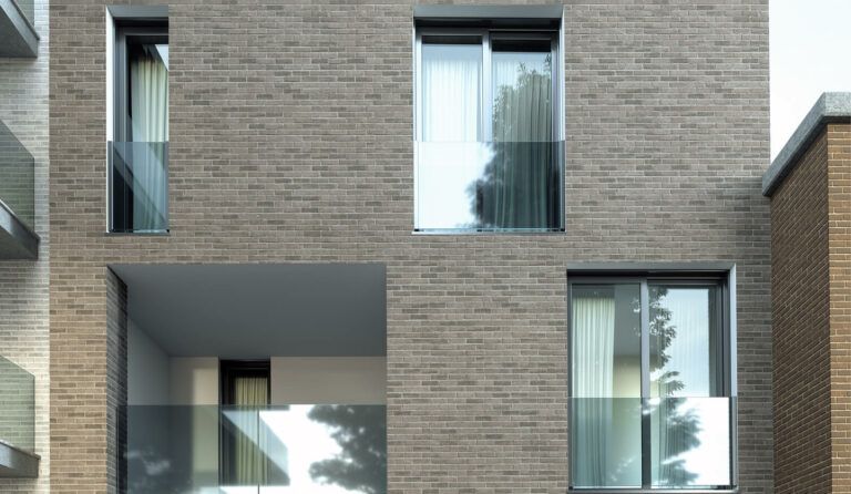 Facciata di un edificio in mattoni con balcone e finestre incassati; un albero si riflette nelle finestre.