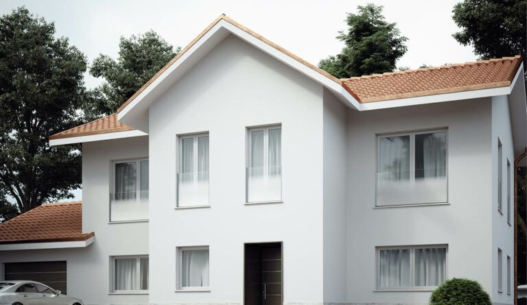 Casa bianca a due piani con tetto di tegole rosse, circondata da alberi verdi.