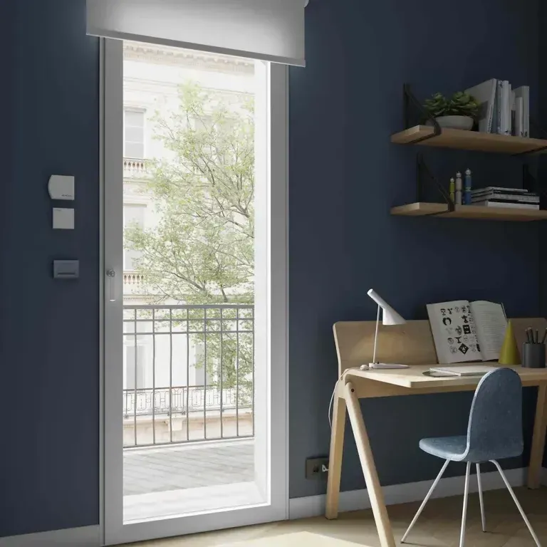 Stanza con pareti blu, scrivania e sedia. Una grande porta a vetri si apre su un balcone alberato.
