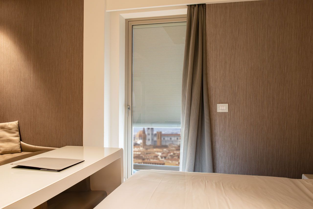 Interno della camera da letto con finestra, scrivania bianca e letto. Carta da parati testurizzata marrone.