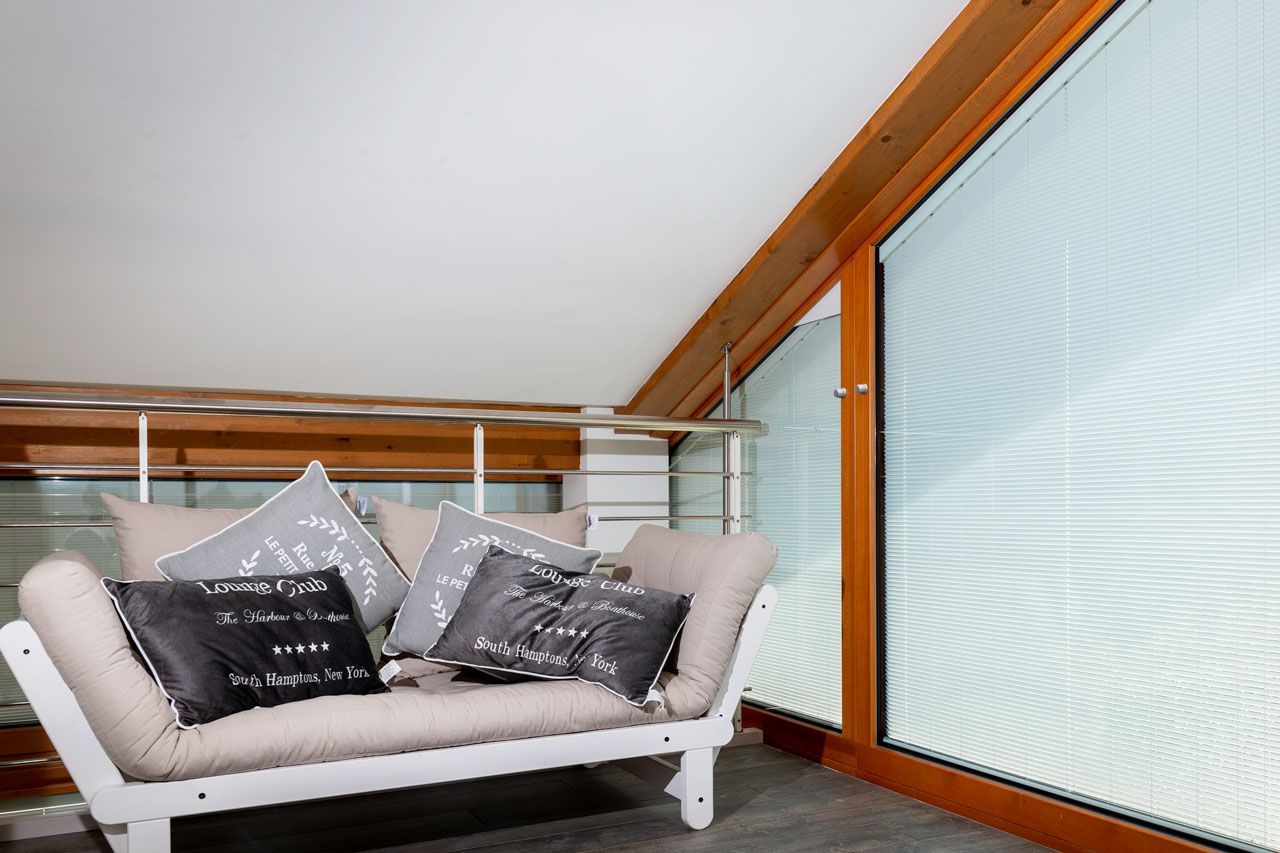 Futon bianco con cuscini vicino a una finestra in un soppalco.