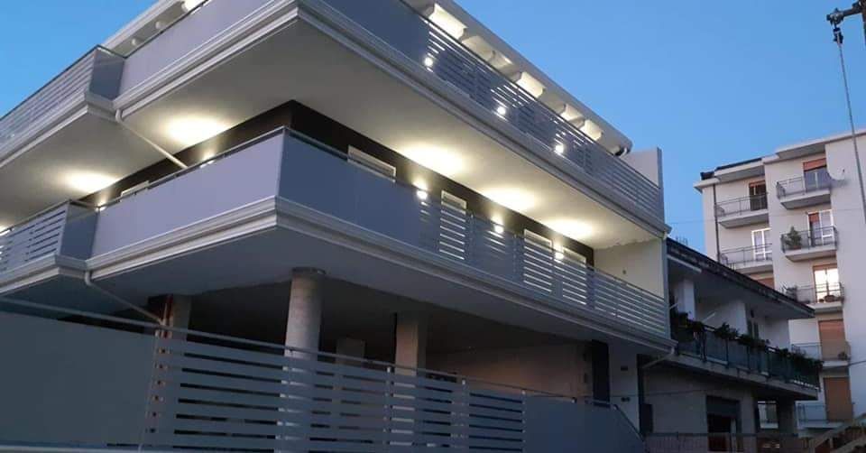 Moderno edificio a più piani con balconi, facciata grigia e bianca, illuminato al tramonto.