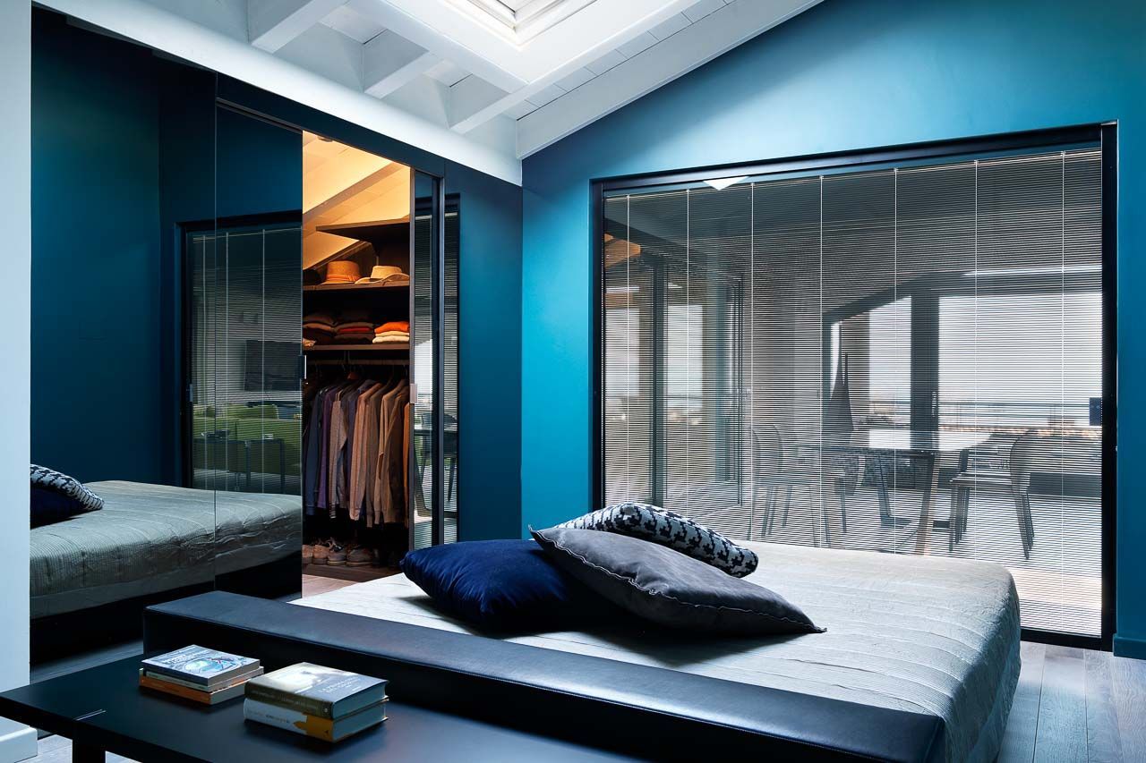Camera da letto con pareti color verde acqua, un letto, un armadio con vestiti e una finestra con le persiane.