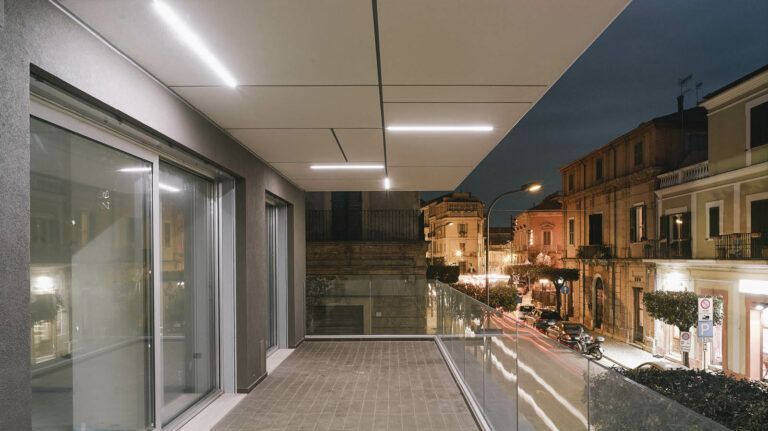 Balcone moderno che si affaccia su una strada di notte, illuminato da luci lineari.