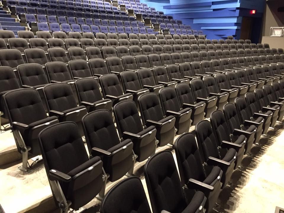 Rows of black seats in an auditorium with a red exit sign