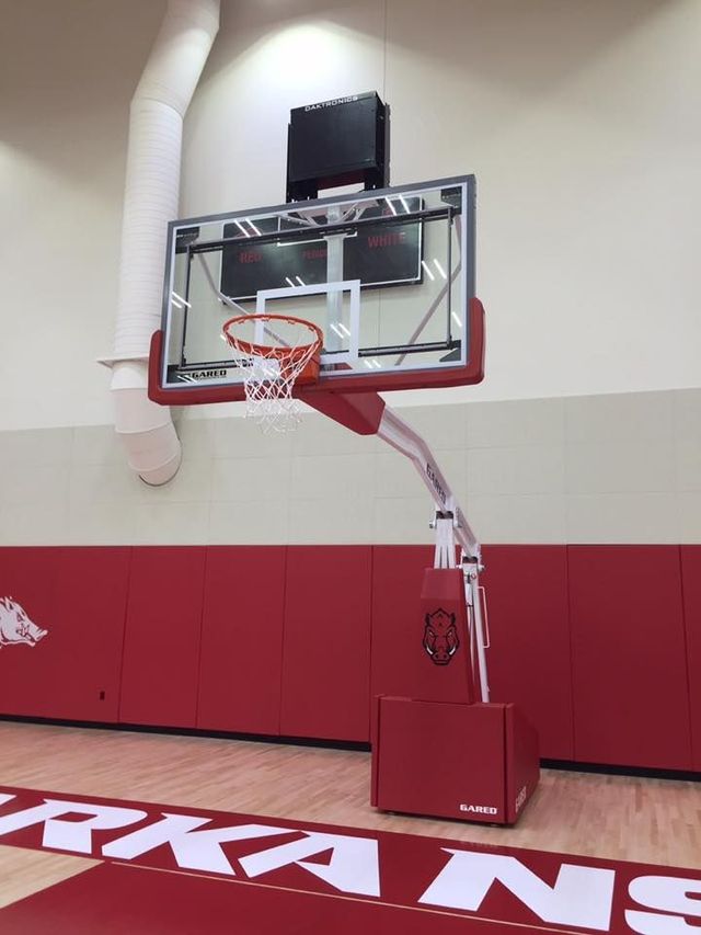 Indoor basketball hoop mounted on a wall in a gym with red padding and a white backboard