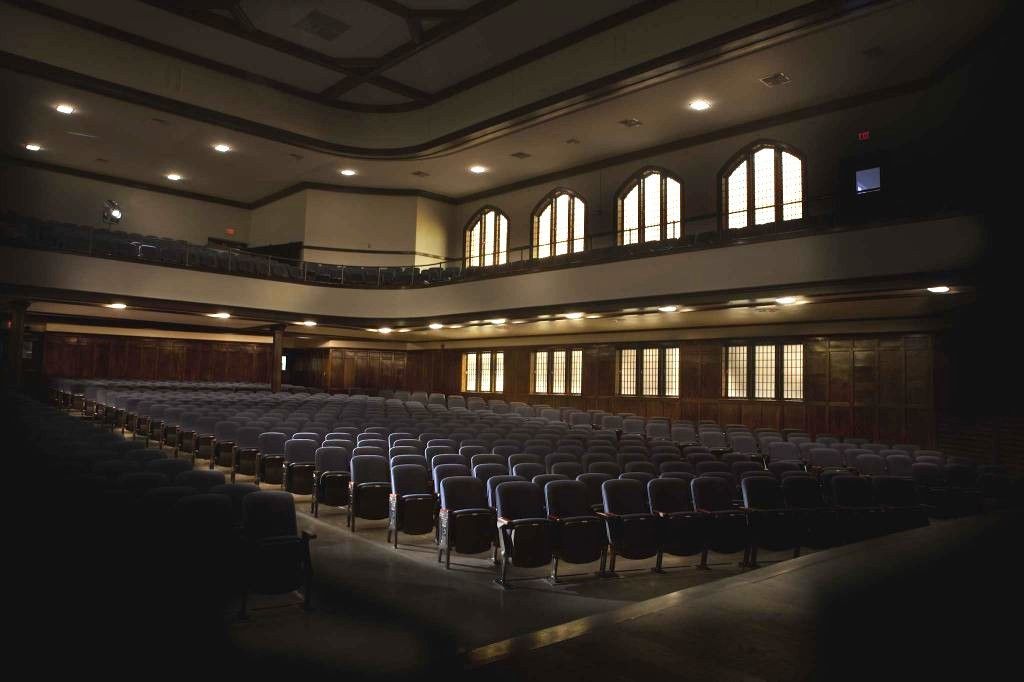 Empty auditorium with rows of chairs and arched windows, softly lit from the side.