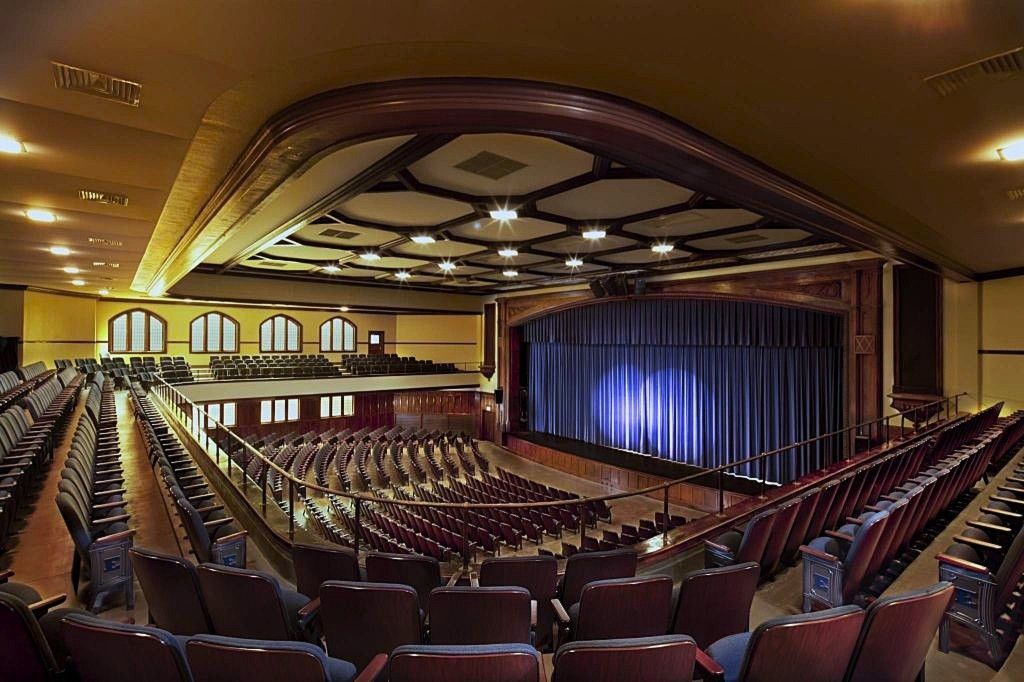 Interior of a grand theater with rows of seats and a stage framed by blue curtains