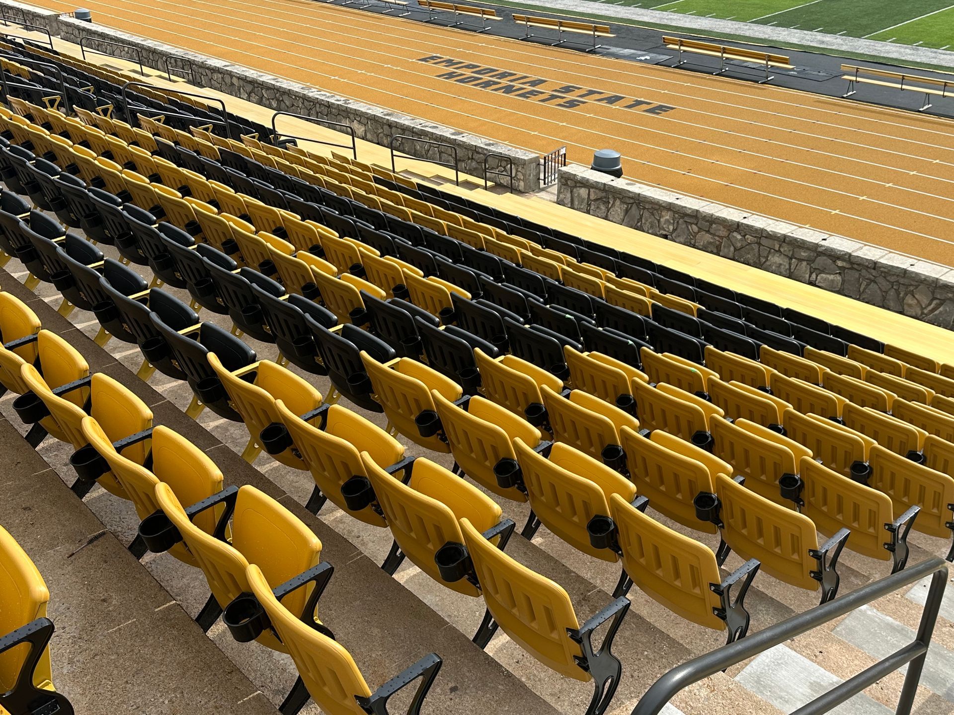Empty yellow stadium seats beside a track field under bright lights