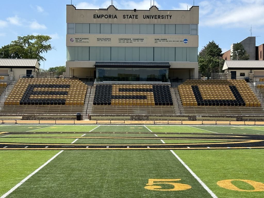 Football stadium stands with gold-and-black seating and Emporia State University sign above the field.