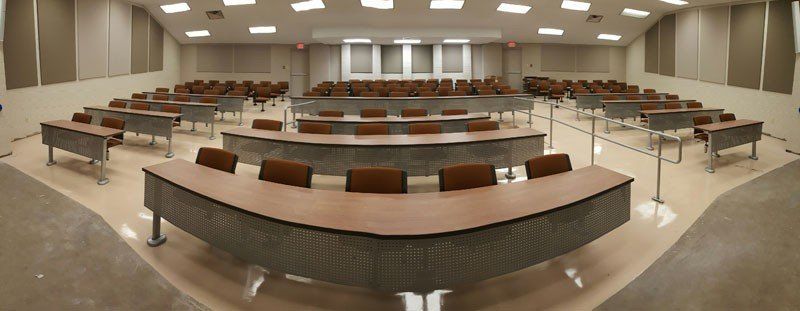 Empty lecture hall with curved rows of desks and beige walls under bright ceiling lights