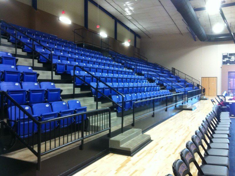 Empty indoor sports bleachers with blue seats and a central aisle.