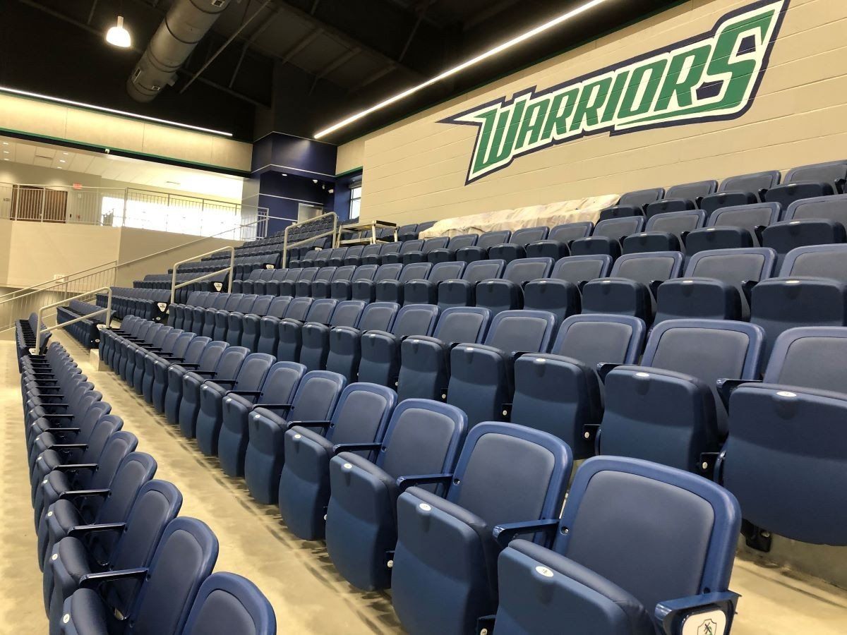 Empty blue stadium seating with a large Warriors logo on the wall.